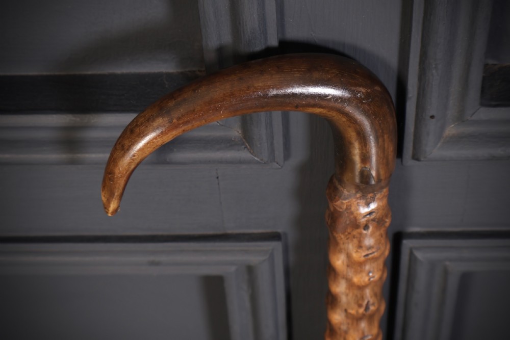 A wooden walking stick featuring a smooth curved crook handle and a textured shaft with natural wood knots. View IV