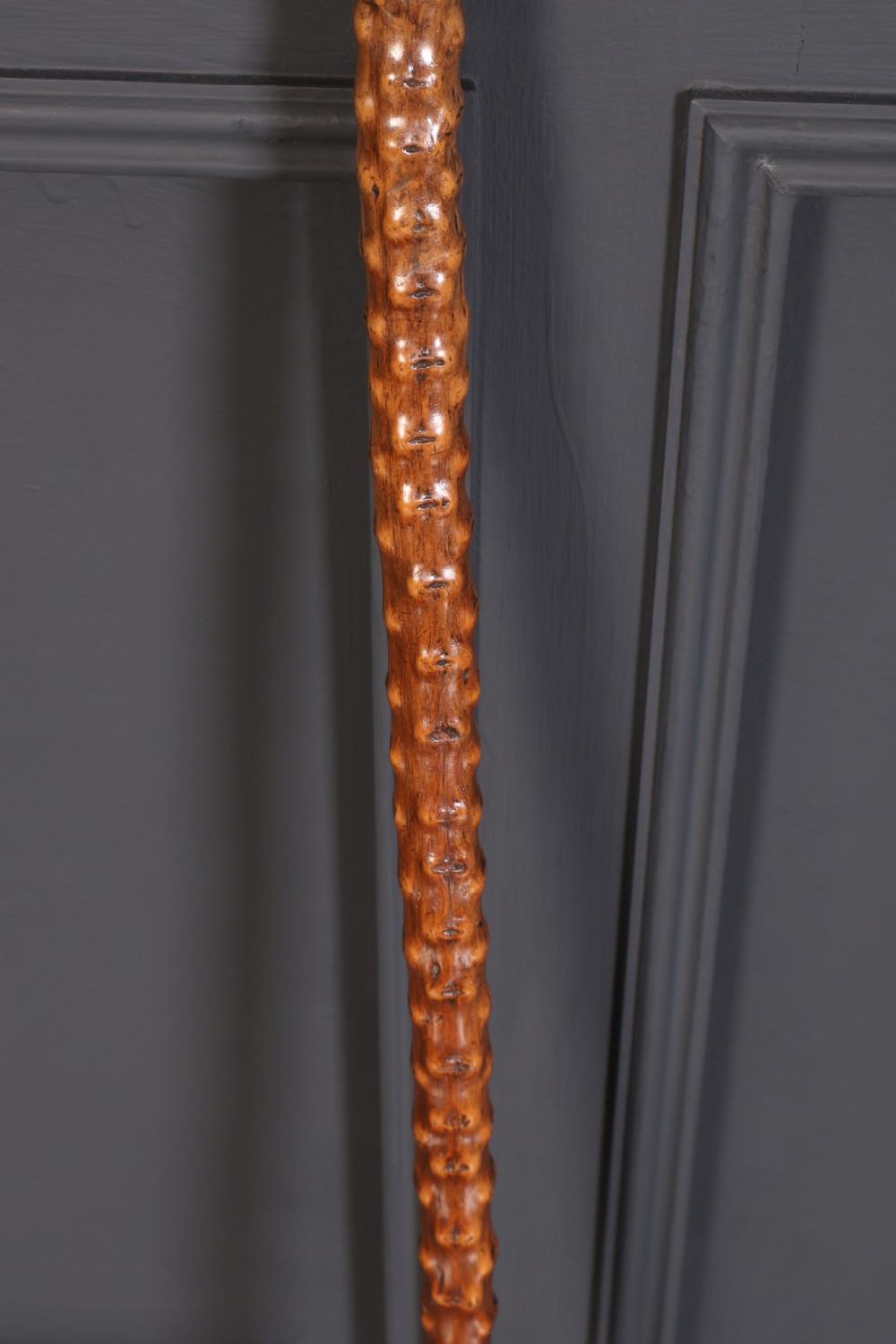 A wooden walking stick featuring a smooth curved crook handle and a textured shaft with natural wood knots. View V
