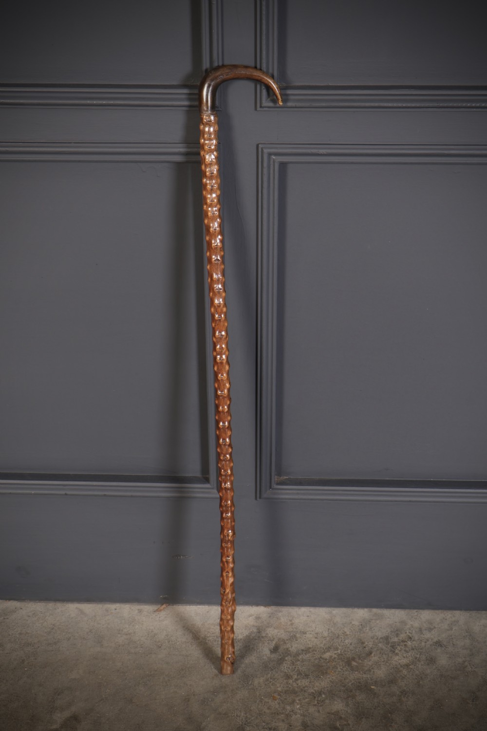 A wooden walking stick featuring a smooth curved crook handle and a textured shaft with natural wood knots. View VI