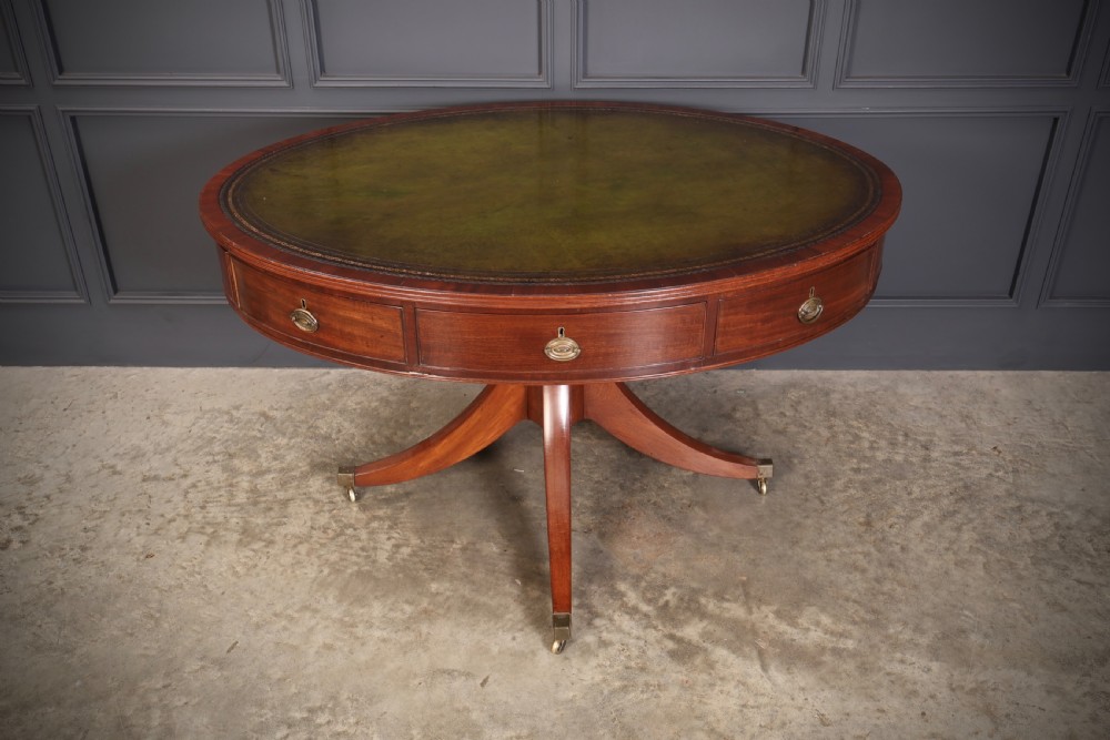 A Georgian mahogany oval drum table with a green leather inset top, frieze drawers with circular brass pulls, and a central pedestal resting on four splayed legs with brass castors.
