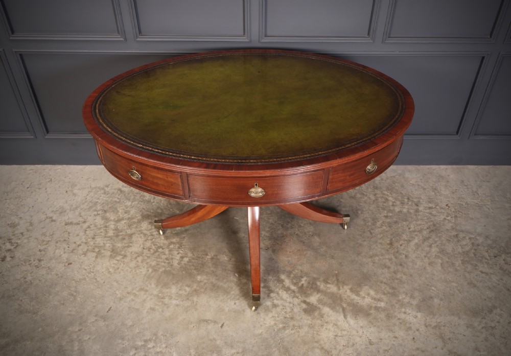 A Georgian mahogany oval drum table with a green leather inset top, frieze drawers with circular brass pulls, and a central pedestal resting on four splayed legs with brass castors. View III