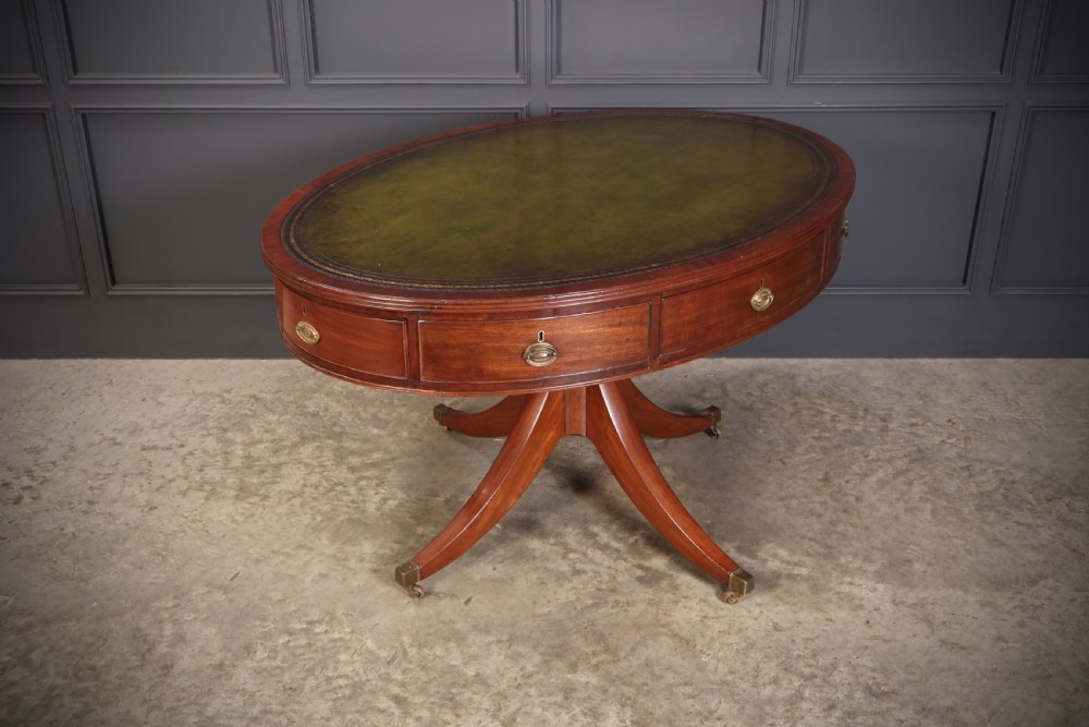 A Georgian mahogany oval drum table with a green leather inset top, frieze drawers with circular brass pulls, and a central pedestal resting on four splayed legs with brass castors. View VI