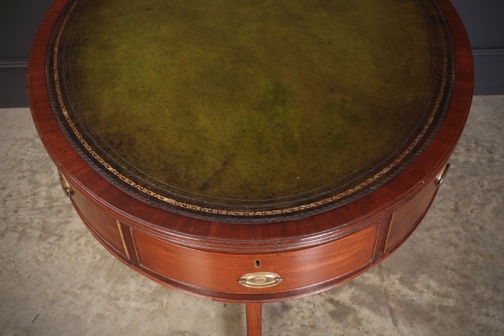 A Georgian mahogany oval drum table with a green leather inset top, frieze drawers with circular brass pulls, and a central pedestal resting on four splayed legs with brass castors. View VIII