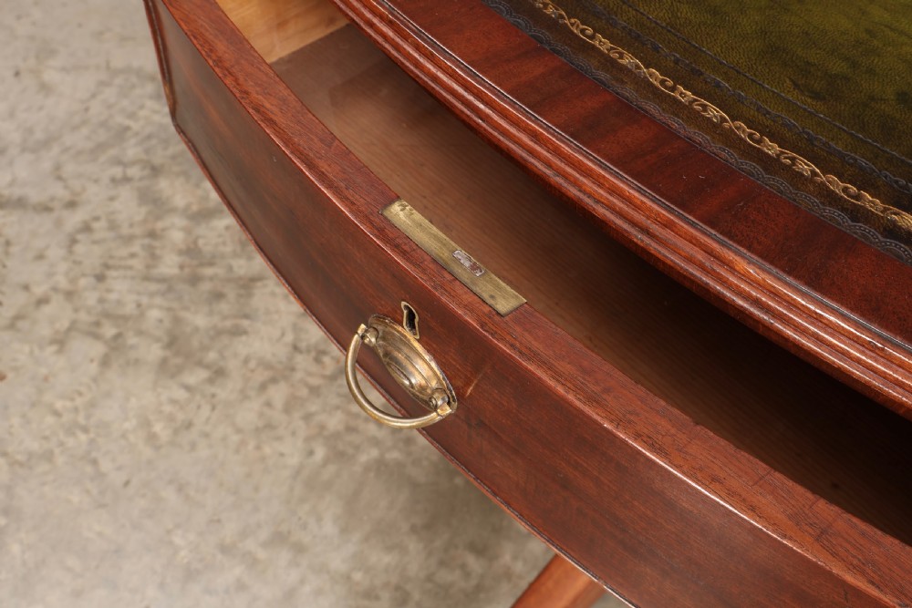 A Georgian mahogany oval drum table with a green leather inset top, frieze drawers with circular brass pulls, and a central pedestal resting on four splayed legs with brass castors. View XII