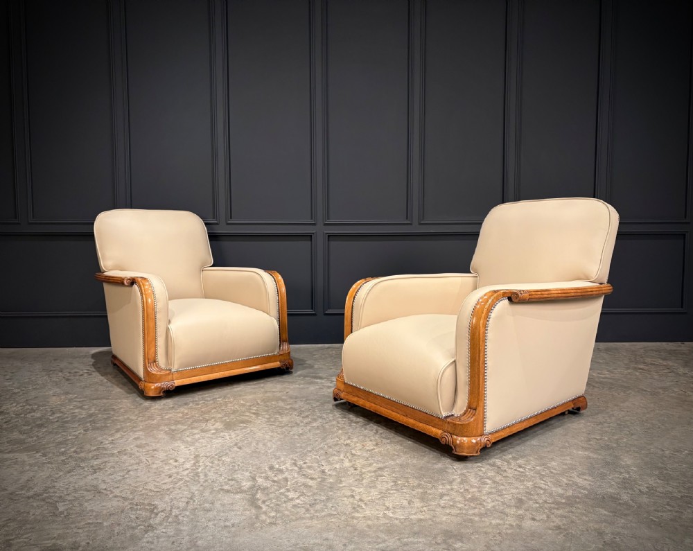 An Art Deco three-piece suite featuring a three-seater sofa and two armchairs upholstered in cream leather with polished walnut trim and stud details. View XXV