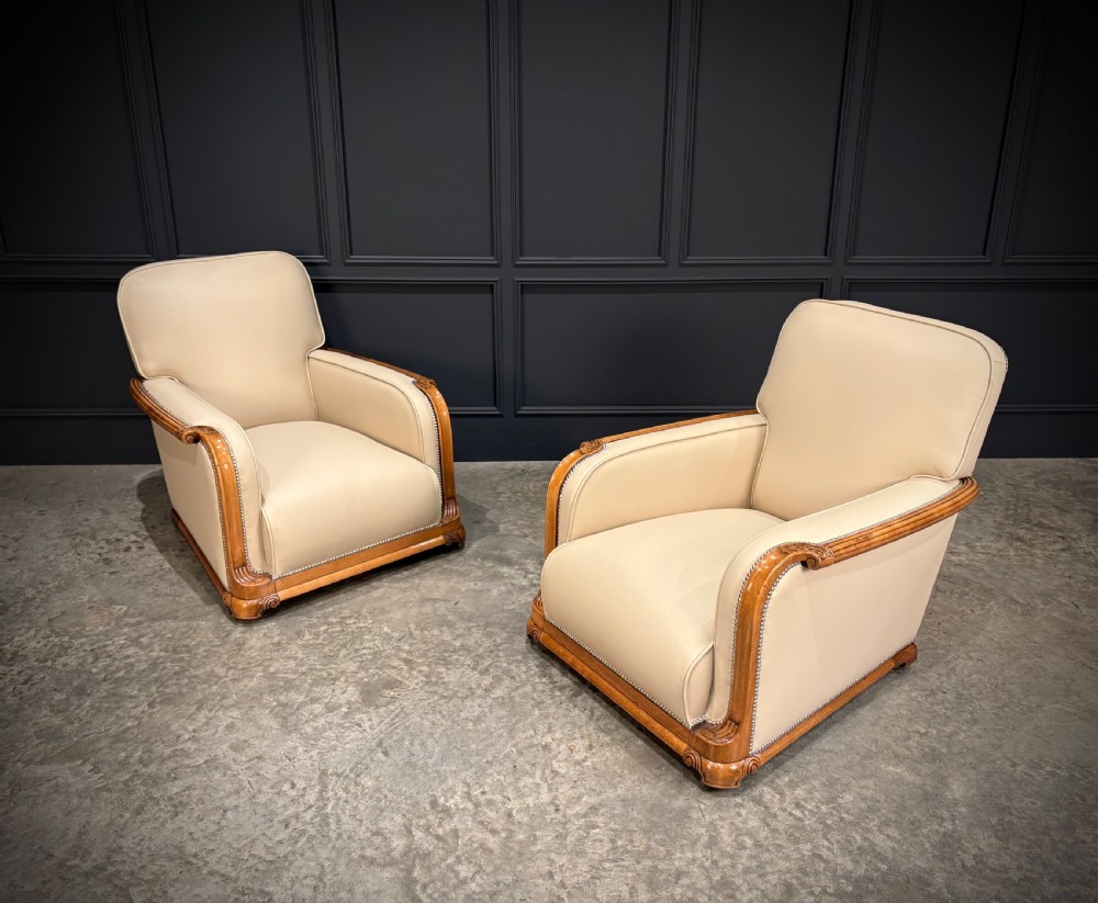An Art Deco three-piece suite featuring a three-seater sofa and two armchairs upholstered in cream leather with polished walnut trim and stud details. View II