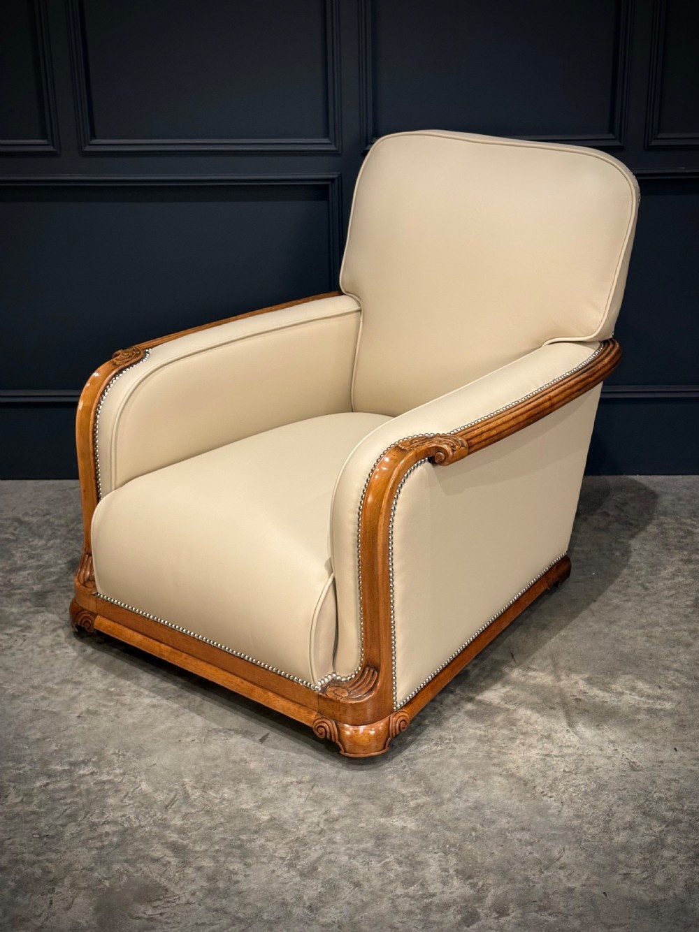 An Art Deco three-piece suite featuring a three-seater sofa and two armchairs upholstered in cream leather with polished walnut trim and stud details. View IX