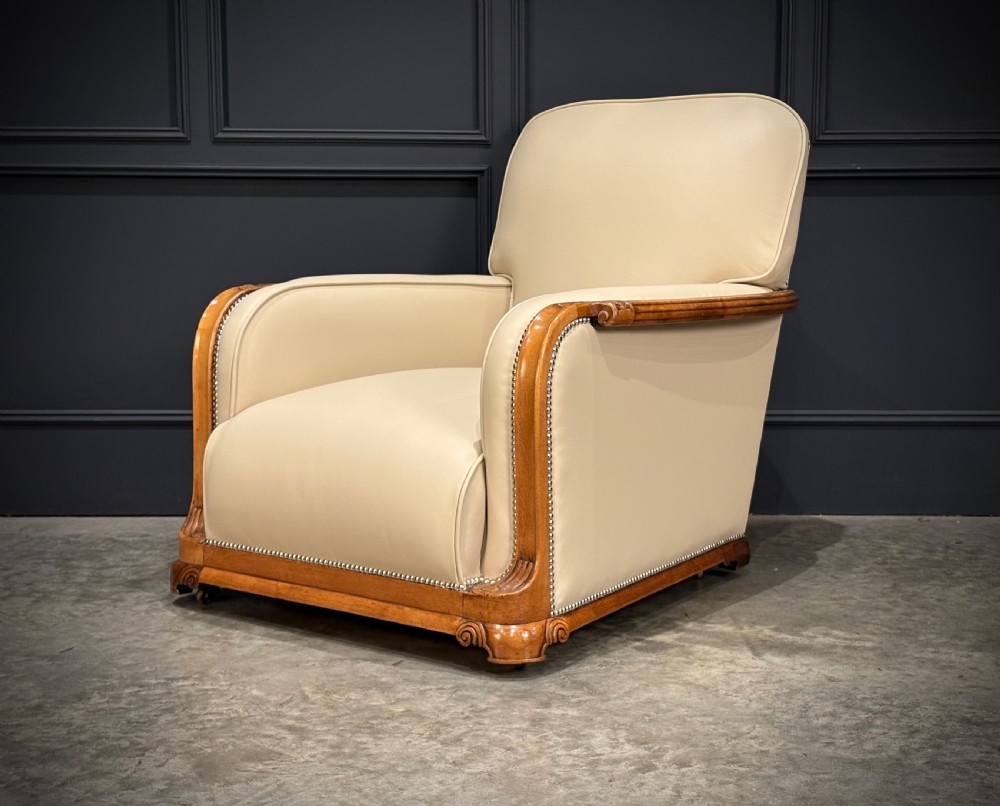 An Art Deco three-piece suite featuring a three-seater sofa and two armchairs upholstered in cream leather with polished walnut trim and stud details. View X