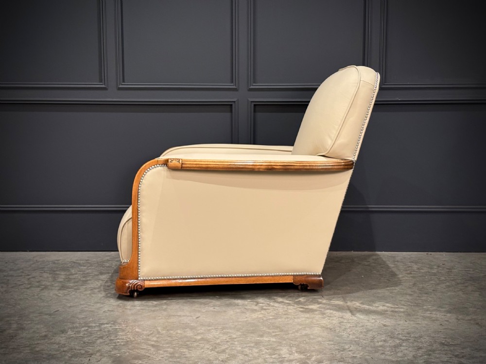 An Art Deco three-piece suite featuring a three-seater sofa and two armchairs upholstered in cream leather with polished walnut trim and stud details. View XI