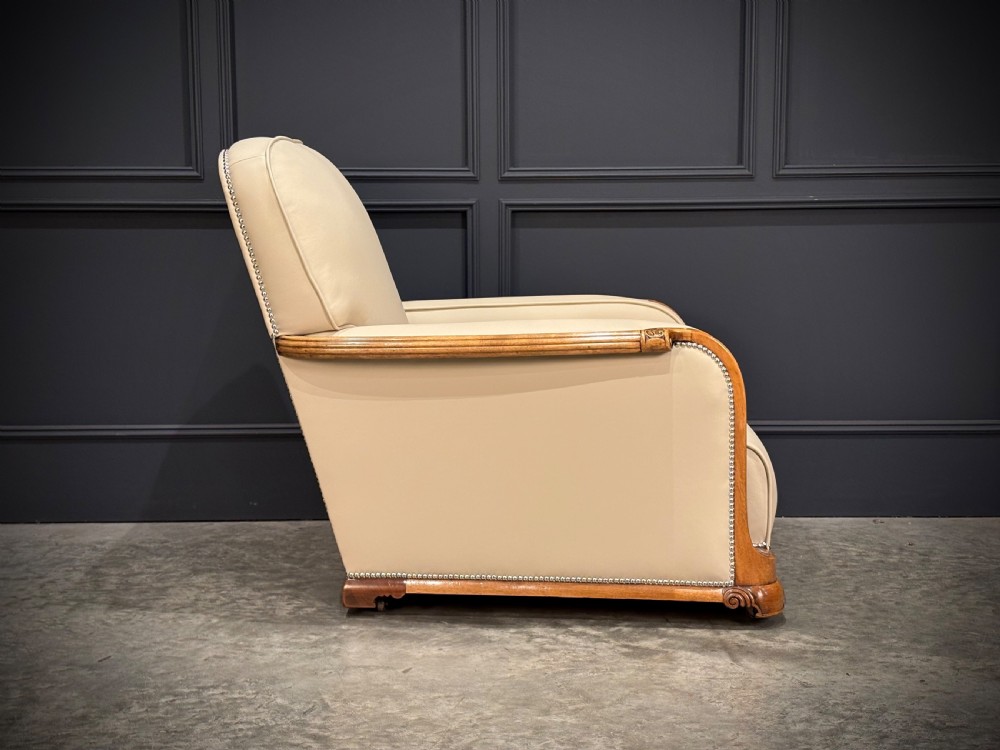 An Art Deco three-piece suite featuring a three-seater sofa and two armchairs upholstered in cream leather with polished walnut trim and stud details. View XIII