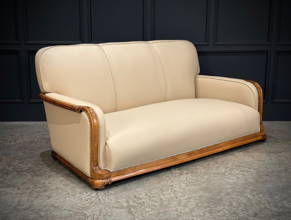 An Art Deco three-piece suite featuring a three-seater sofa and two armchairs upholstered in cream leather with polished walnut trim and stud details. View XIV