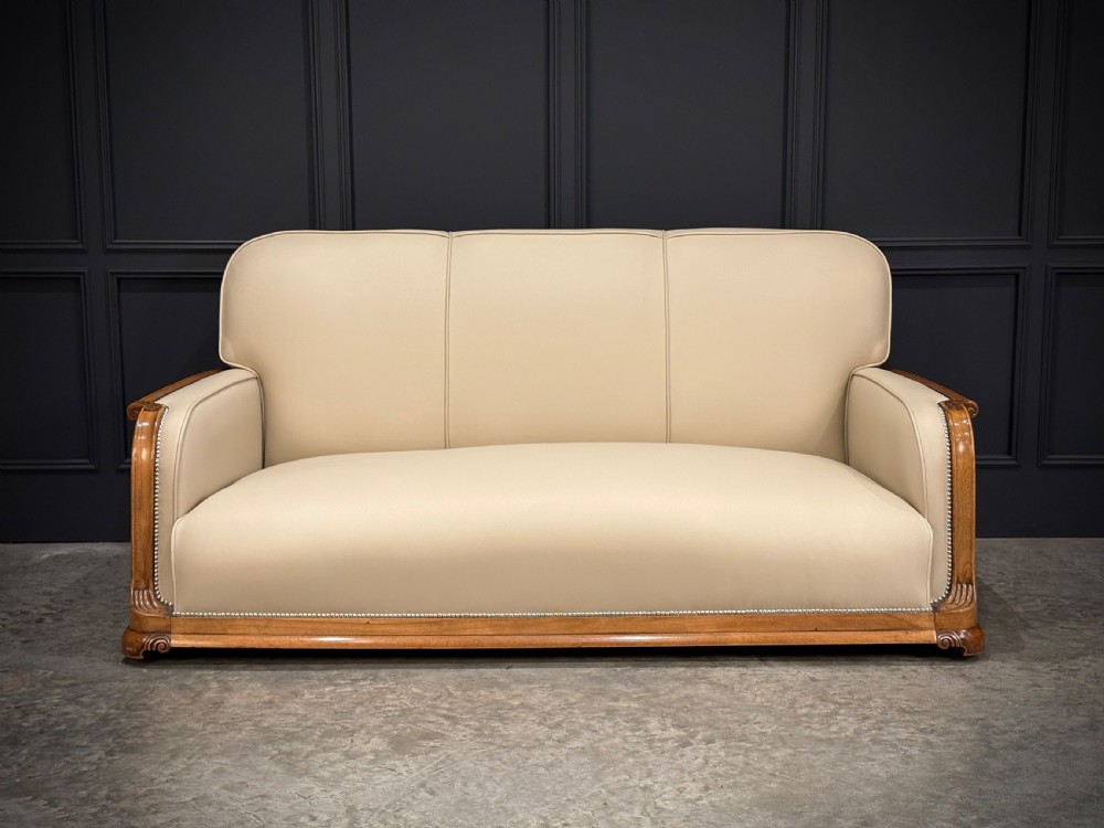 An Art Deco three-piece suite featuring a three-seater sofa and two armchairs upholstered in cream leather with polished walnut trim and stud details. View XVI