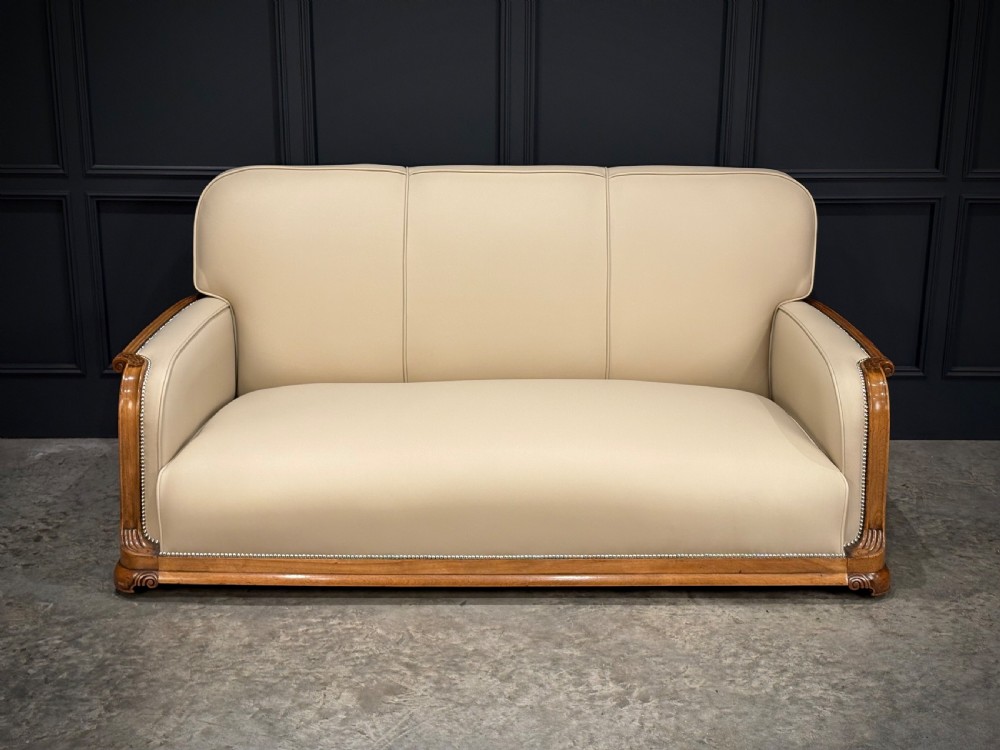 An Art Deco three-piece suite featuring a three-seater sofa and two armchairs upholstered in cream leather with polished walnut trim and stud details. View XVII