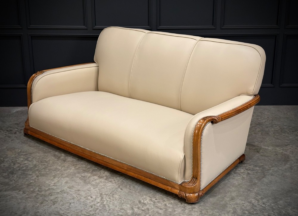 An Art Deco three-piece suite featuring a three-seater sofa and two armchairs upholstered in cream leather with polished walnut trim and stud details. View XIX