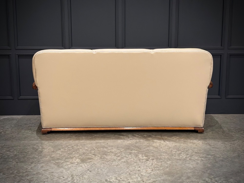 An Art Deco three-piece suite featuring a three-seater sofa and two armchairs upholstered in cream leather with polished walnut trim and stud details. View XXII