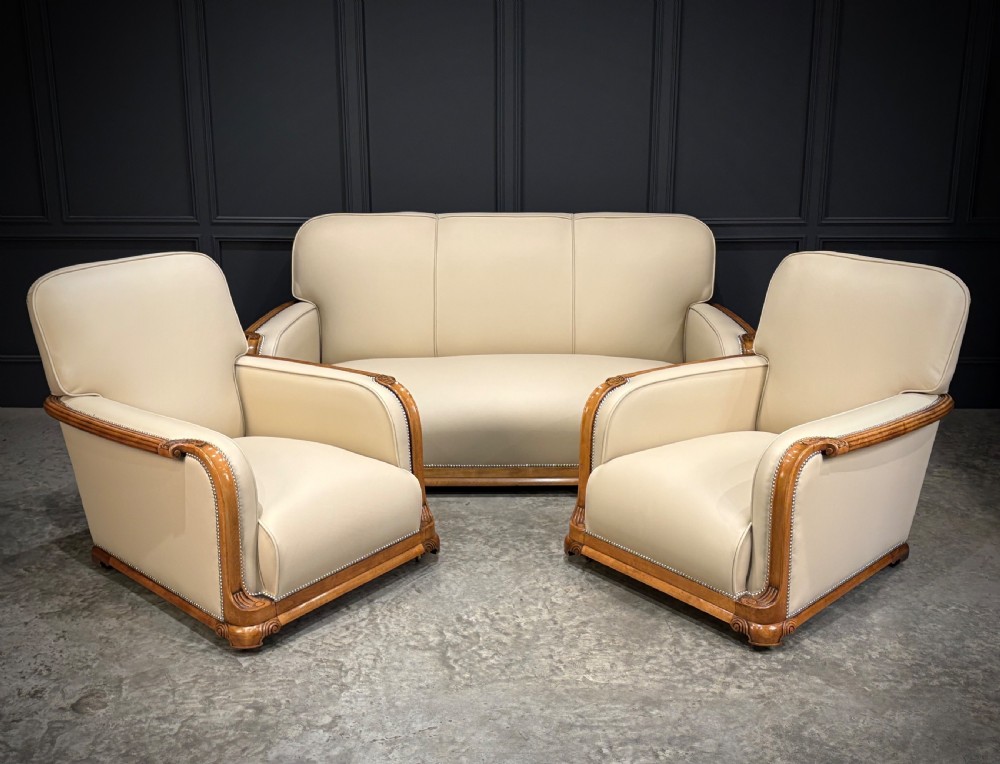 An Art Deco three-piece suite featuring a three-seater sofa and two armchairs upholstered in cream leather with polished walnut trim and stud details. View XXIII