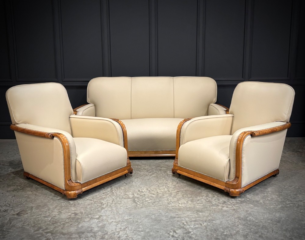 An Art Deco three-piece suite featuring a three-seater sofa and two armchairs upholstered in cream leather with polished walnut trim and stud details. View XXIV
