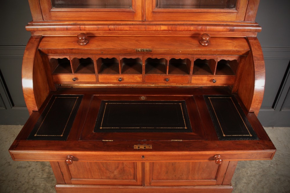 A Victorian warm brown walnut cylinder bureau bookcase featuring a two-door glazed upper cabinet over a curved roll-top desk section and lower cupboard base. View V