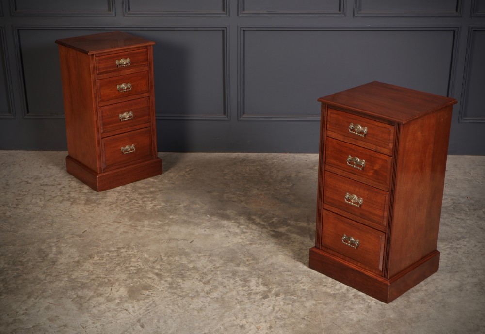 A pair of late Victorian walnut bedside chests, each featuring four drawers with ornamental brass handles on a plinth base.