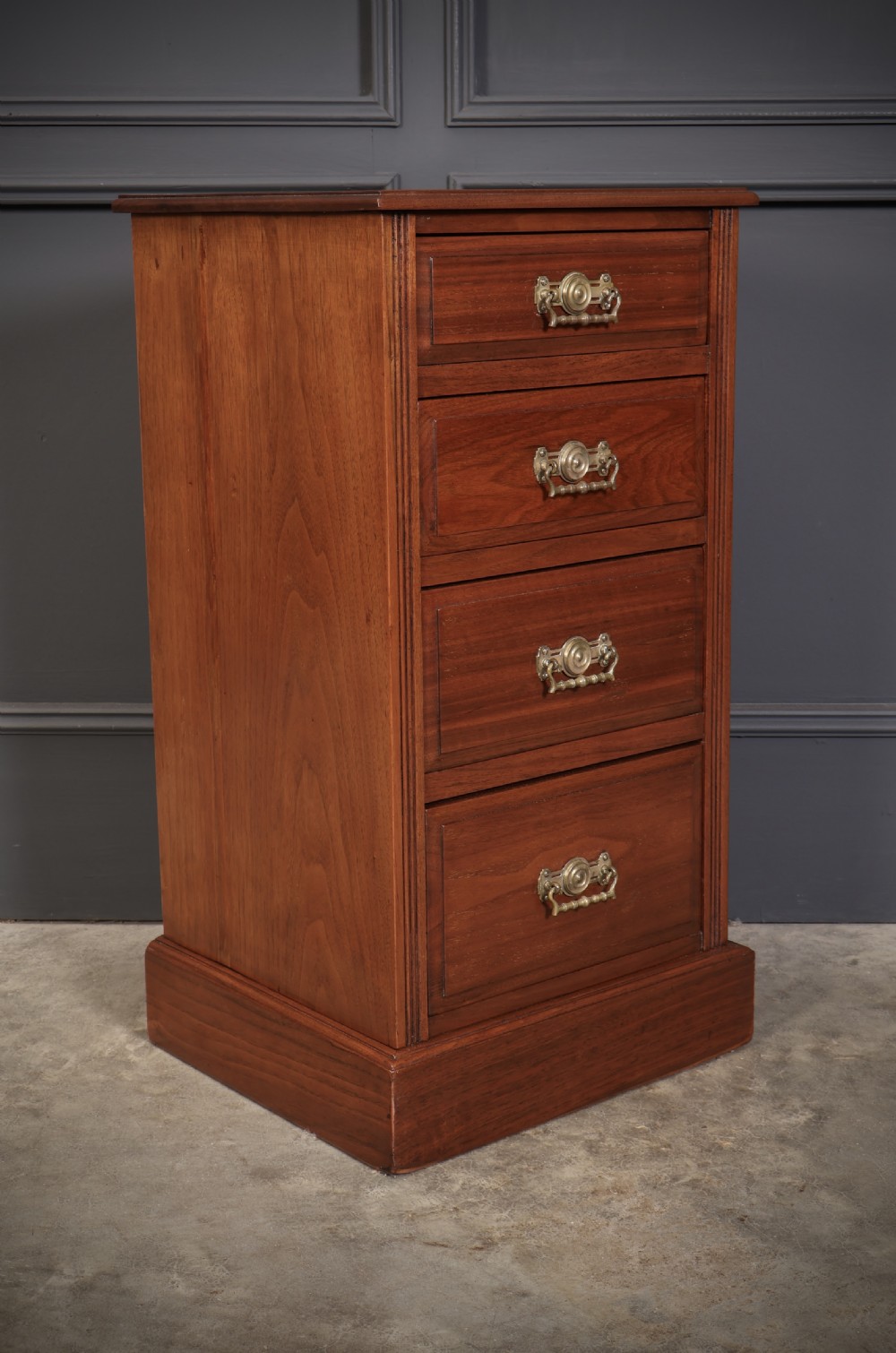 A pair of late Victorian walnut bedside chests, each featuring four drawers with ornamental brass handles on a plinth base. View V