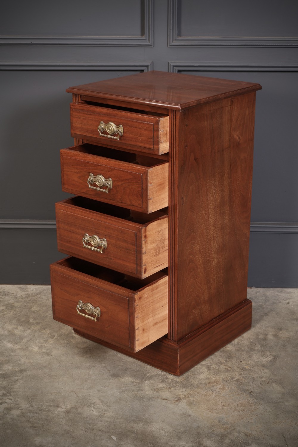 A pair of late Victorian walnut bedside chests, each featuring four drawers with ornamental brass handles on a plinth base. View IX