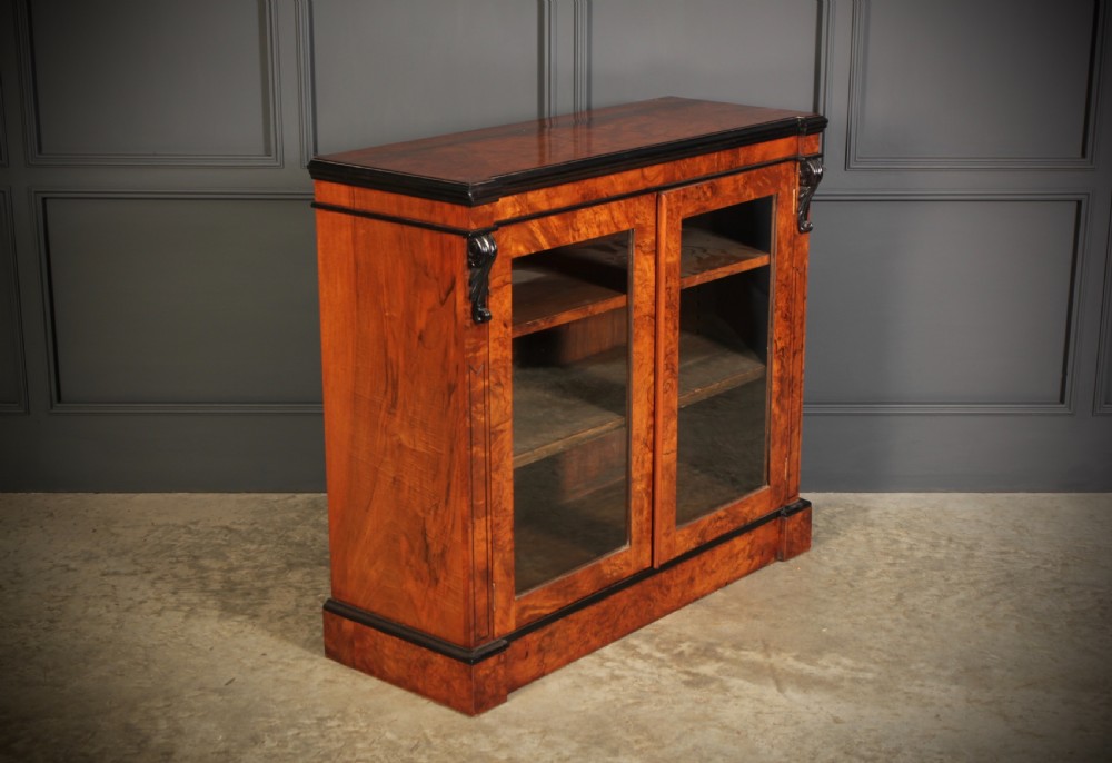 A low Victorian bookcase constructed from figured walnut wood featuring two glazed glass doors, black carved corbels, and internal timber shelves. View II
