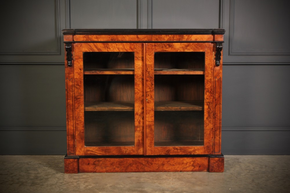 A low Victorian bookcase constructed from figured walnut wood featuring two glazed glass doors, black carved corbels, and internal timber shelves. View III