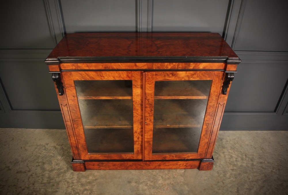A low Victorian bookcase constructed from figured walnut wood featuring two glazed glass doors, black carved corbels, and internal timber shelves. View V
