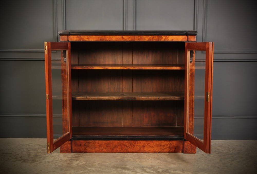 A low Victorian bookcase constructed from figured walnut wood featuring two glazed glass doors, black carved corbels, and internal timber shelves. View VI