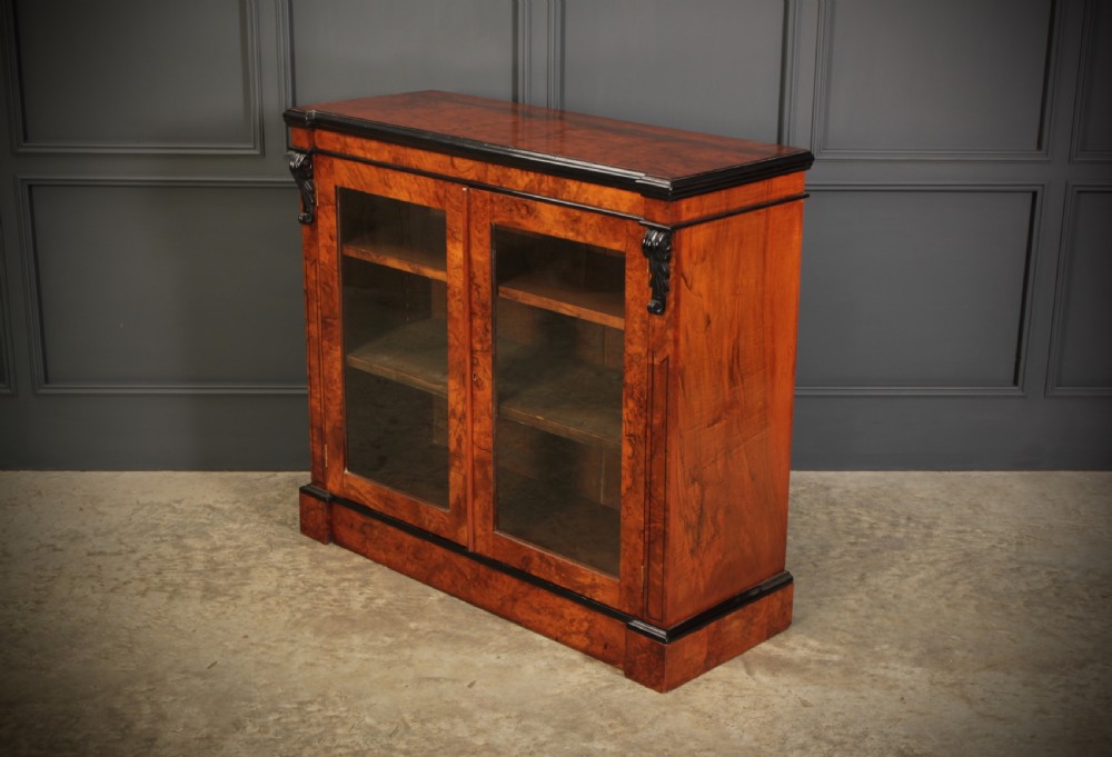 A low Victorian bookcase constructed from figured walnut wood featuring two glazed glass doors, black carved corbels, and internal timber shelves. View VII