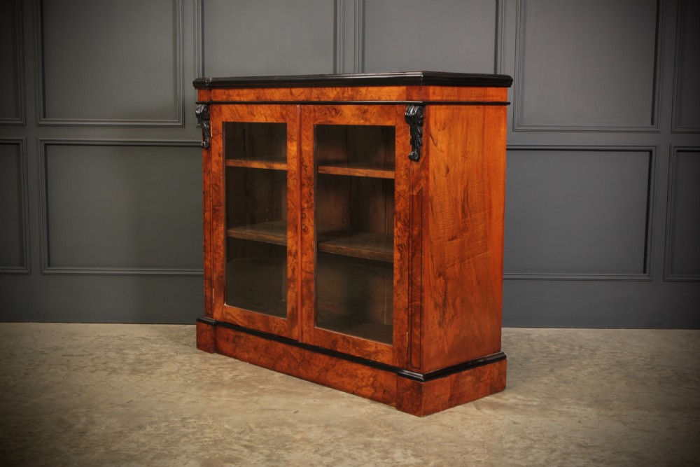 A low Victorian bookcase constructed from figured walnut wood featuring two glazed glass doors, black carved corbels, and internal timber shelves. View VIII