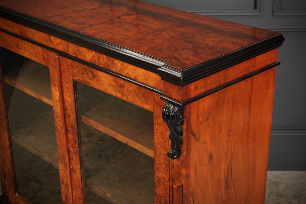 A low Victorian bookcase constructed from figured walnut wood featuring two glazed glass doors, black carved corbels, and internal timber shelves. View IX