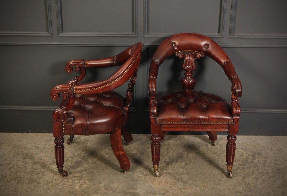 A pair of William IV rosewood desk chairs featuring deep buttoned reddish-brown leather upholstery, carved scroll arms, turned front legs with brass castors, and splayed rear legs. View XVIII