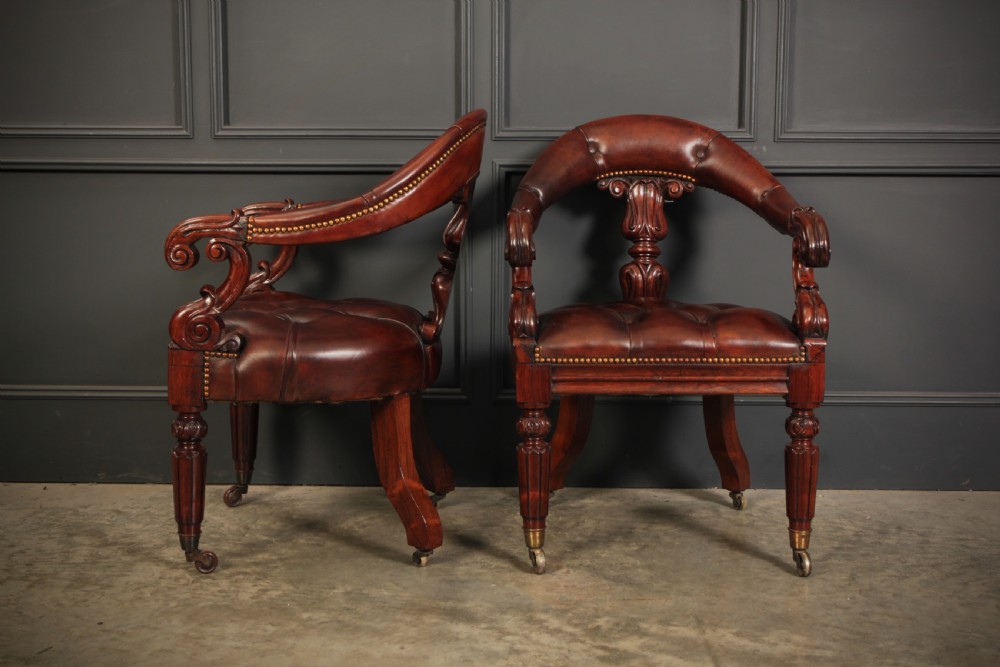 A pair of William IV rosewood desk chairs featuring deep buttoned reddish-brown leather upholstery, carved scroll arms, turned front legs with brass castors, and splayed rear legs. View XIX