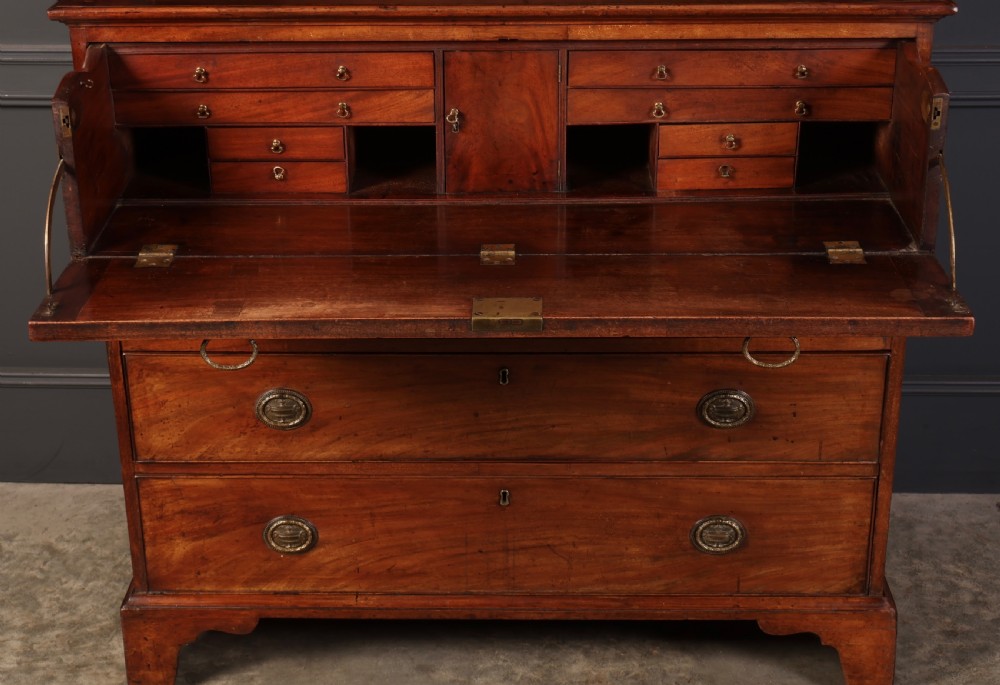 A George III mahogany secretaire cabinet featuring a twin panelled cupboard top over a lower chest of drawers with bracket feet. View VI