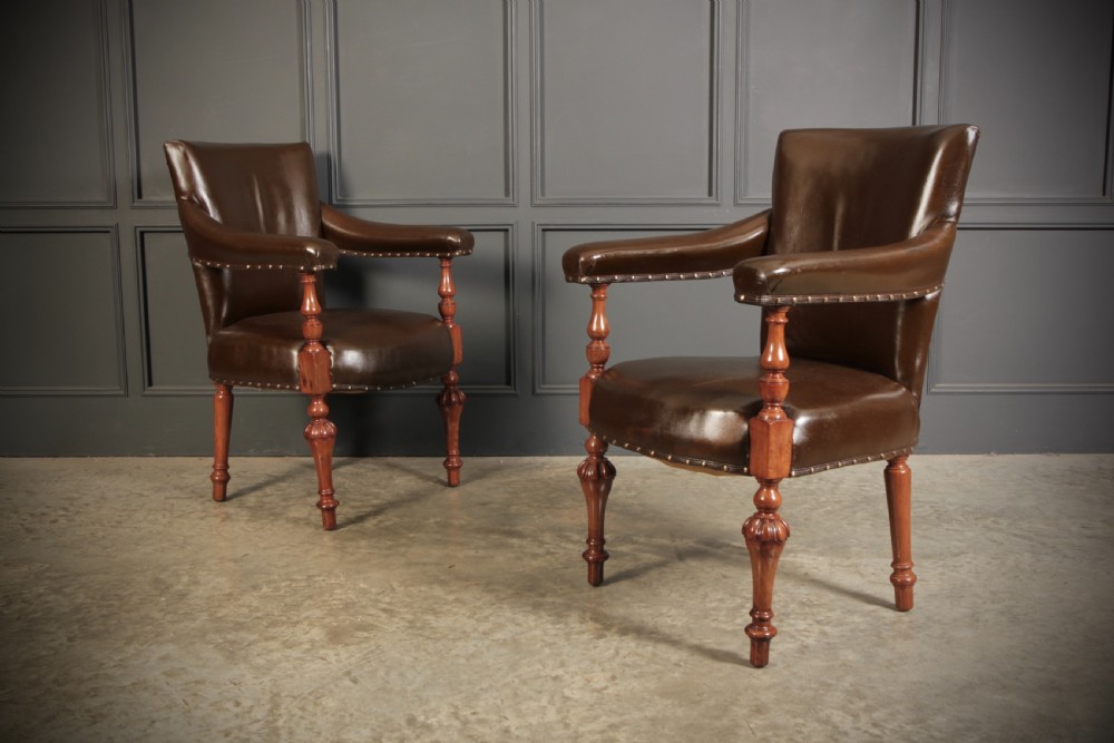 A pair of Victorian mahogany library armchairs upholstered in dark brown leather with brass studding and turned front legs.