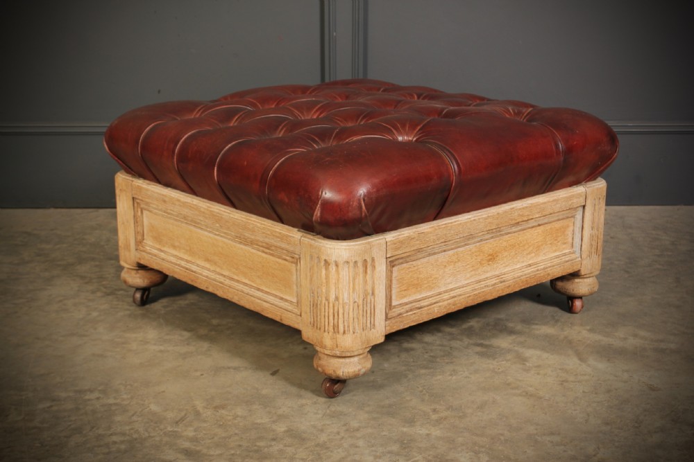 A large square Victorian footstool with deep-buttoned reddish-brown leather upholstery set within a carved light oak frame on castors. View II