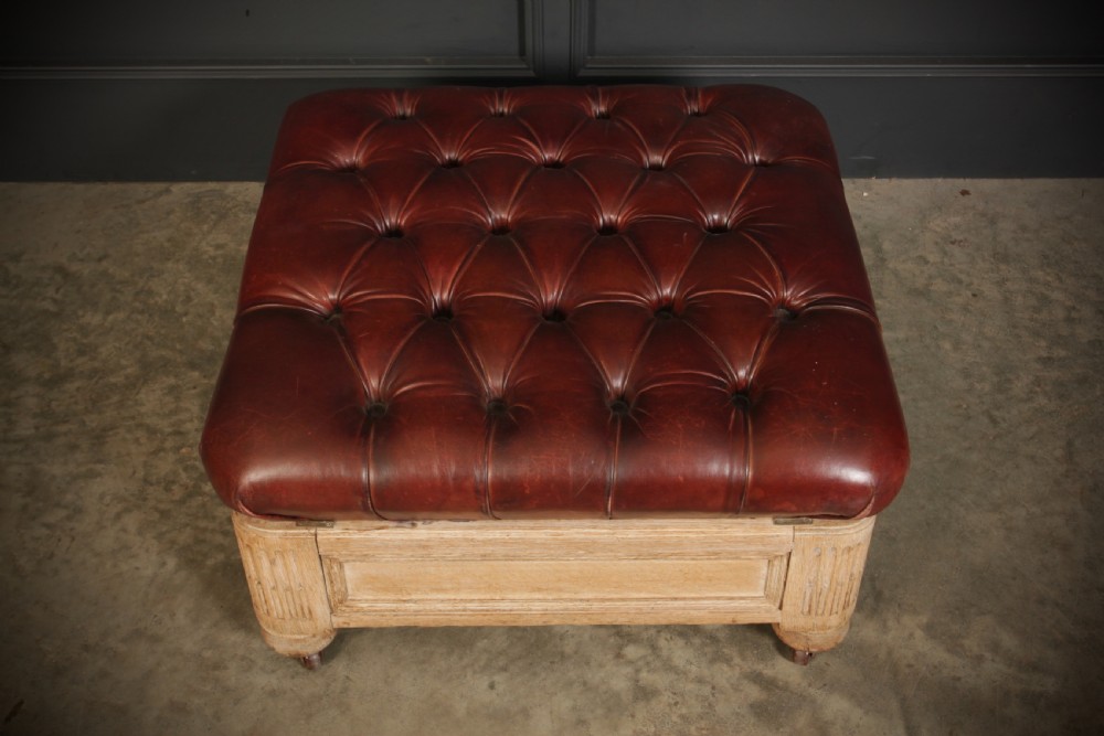 A large square Victorian footstool with deep-buttoned reddish-brown leather upholstery set within a carved light oak frame on castors. View V