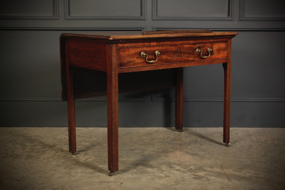 A Georgian mahogany architects table with a hinged adjustable writing slope top, a single drawer with brass swan-neck handles, and straight square legs fitted with brass castors.