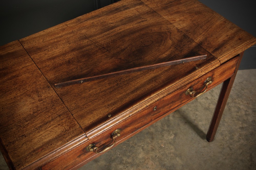 A Georgian mahogany architects table with a hinged adjustable writing slope top, a single drawer with brass swan-neck handles, and straight square legs fitted with brass castors. View IX