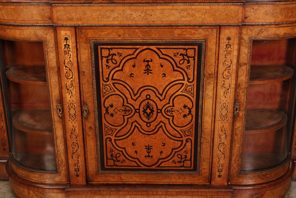 A nineteenth-century Victorian credenza made from burr walnut featuring central floral marquetry, curved glazed side display doors, and polished metal mounts. View VI
