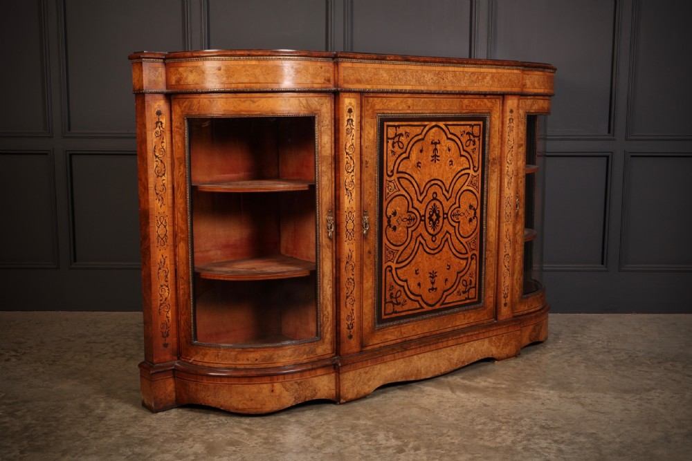 A nineteenth-century Victorian credenza made from burr walnut featuring central floral marquetry, curved glazed side display doors, and polished metal mounts. View V