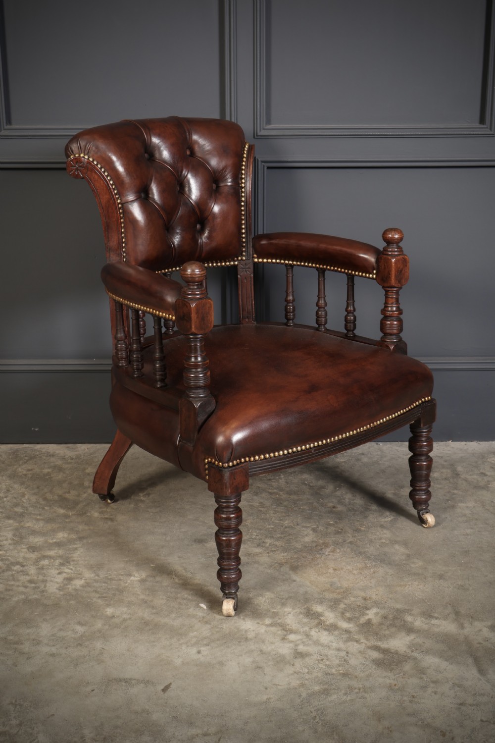 A pair of Victorian mahogany captains desk chairs upholstered in buttoned brown leather with stud detailing and turned legs on castors. View II