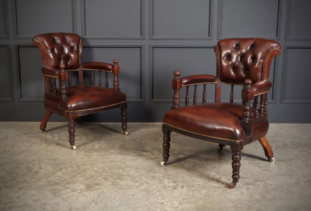 A pair of Victorian mahogany captains desk chairs upholstered in buttoned brown leather with stud detailing and turned legs on castors.