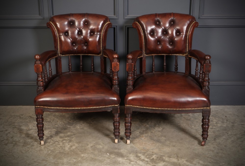 A pair of Victorian mahogany captains desk chairs upholstered in buttoned brown leather with stud detailing and turned legs on castors. View V