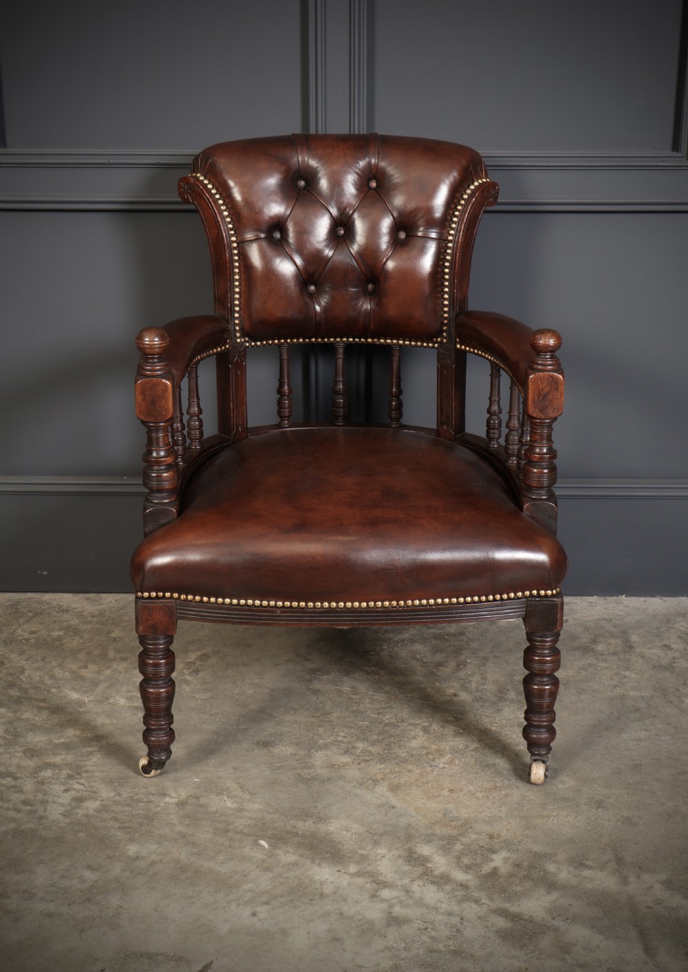 A pair of Victorian mahogany captains desk chairs upholstered in buttoned brown leather with stud detailing and turned legs on castors. View VI