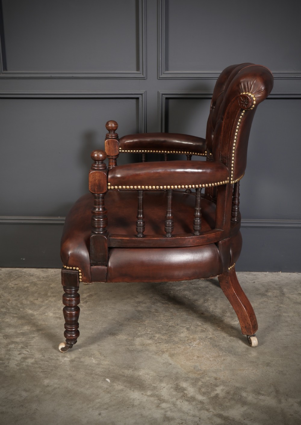 A pair of Victorian mahogany captains desk chairs upholstered in buttoned brown leather with stud detailing and turned legs on castors. View X