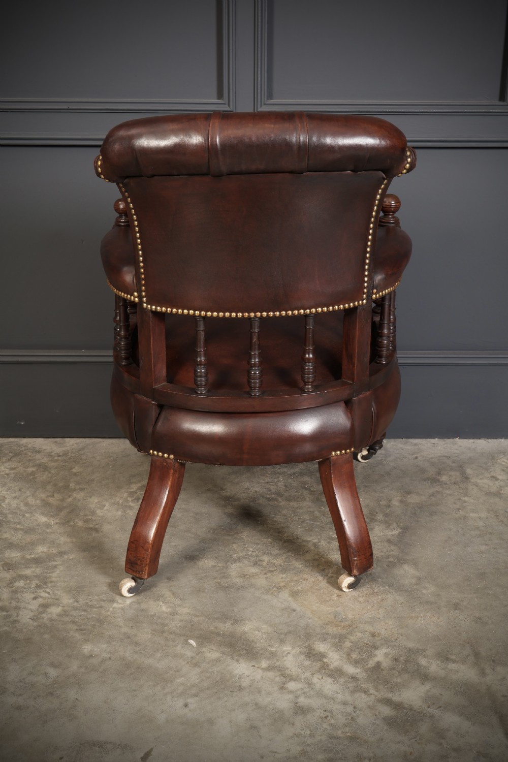 A pair of Victorian mahogany captains desk chairs upholstered in buttoned brown leather with stud detailing and turned legs on castors. View XI