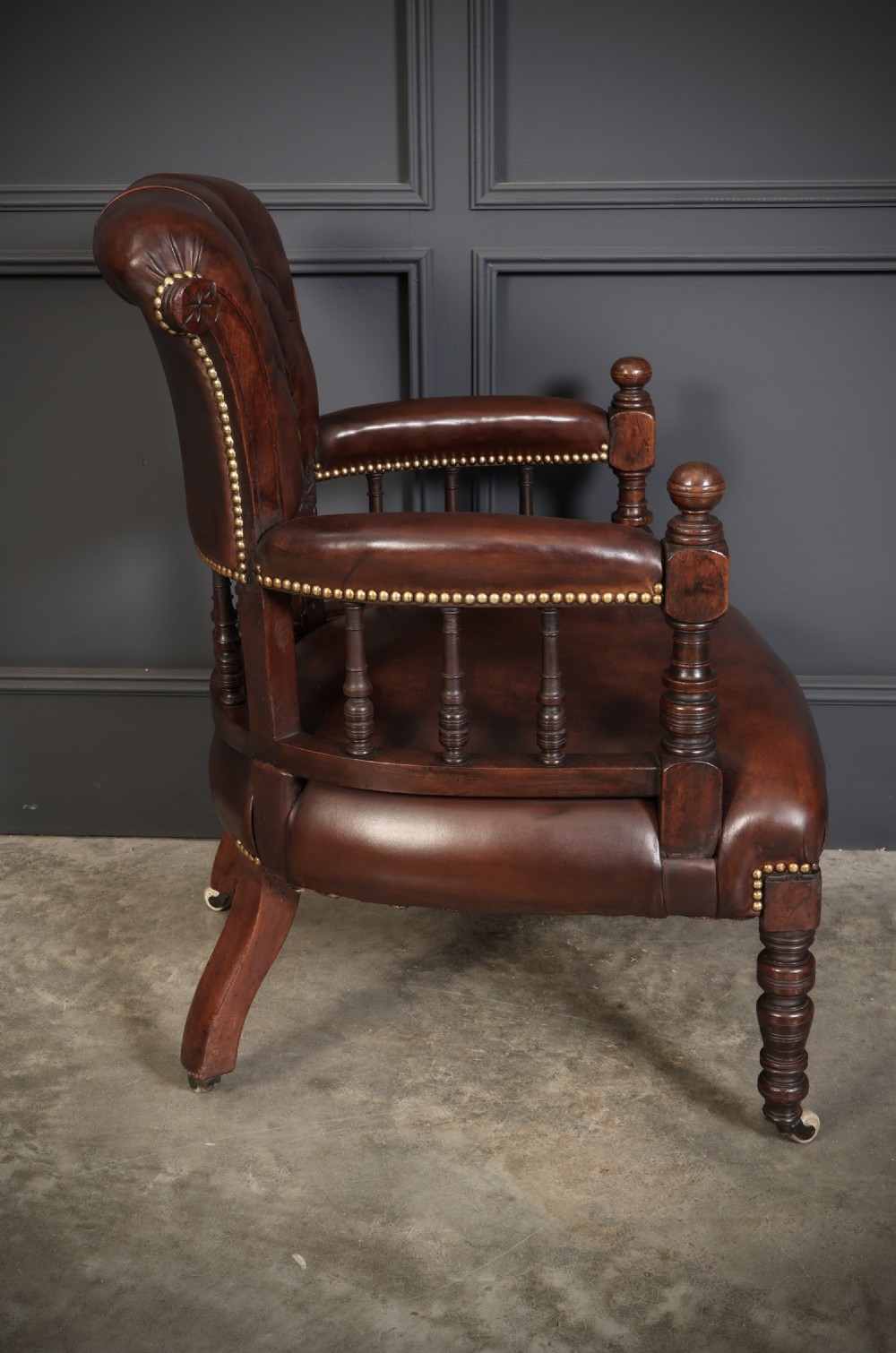 A pair of Victorian mahogany captains desk chairs upholstered in buttoned brown leather with stud detailing and turned legs on castors. View XII