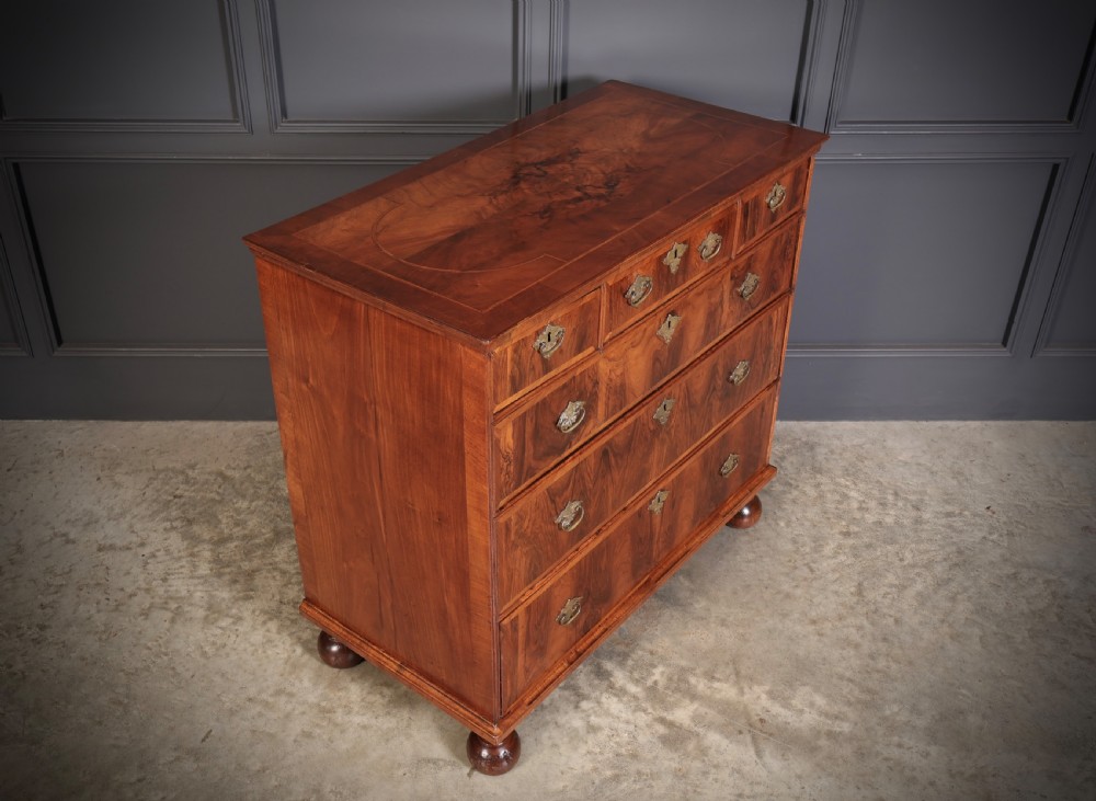 A Queen Anne style warm brown walnut chest of drawers featuring inlaid geometric top decoration, brass drop handles, keyhole escutcheons, and turned bun feet. View II
